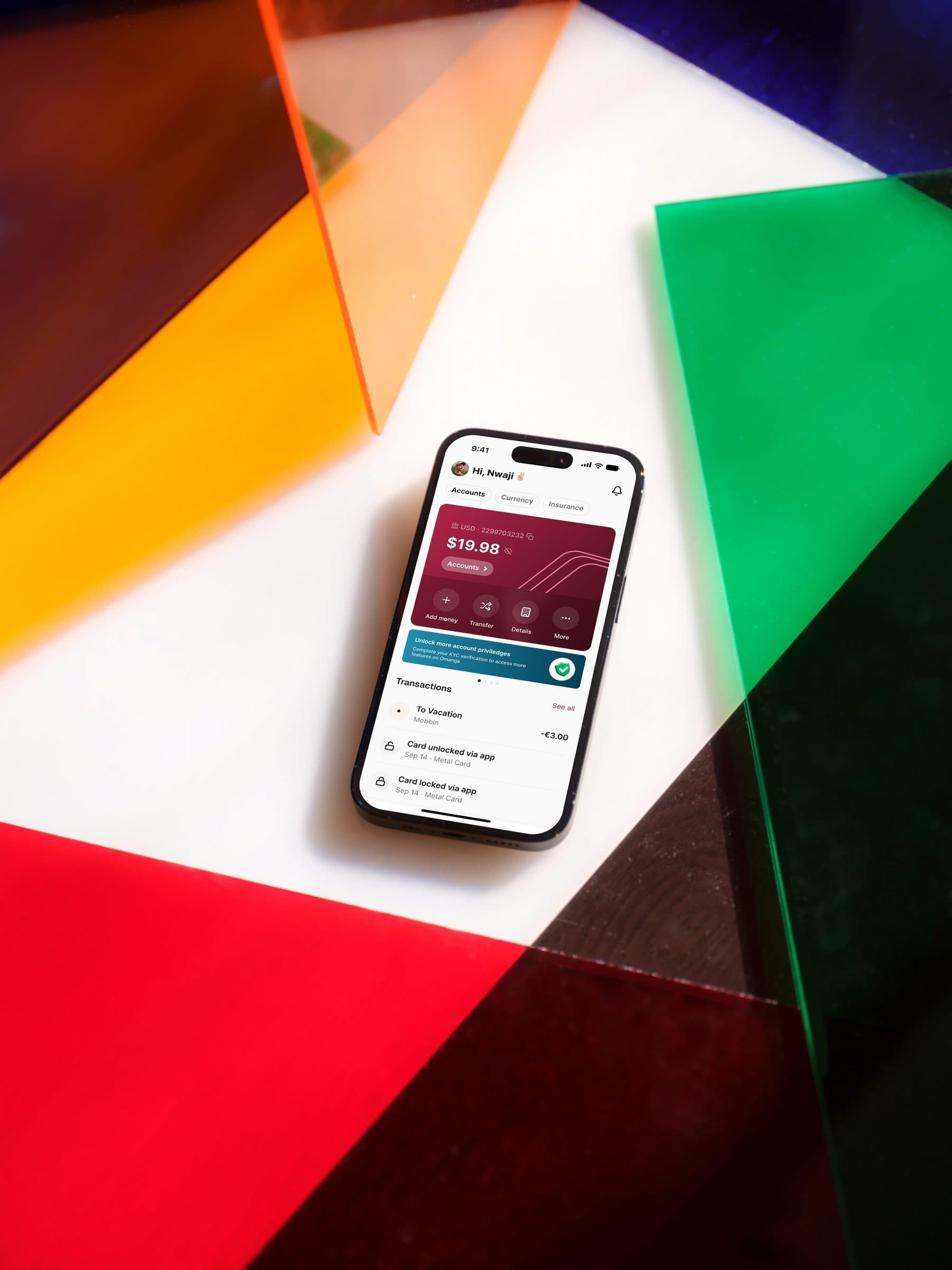 The Omanga app open on a phone resting on panels of coloured glass.